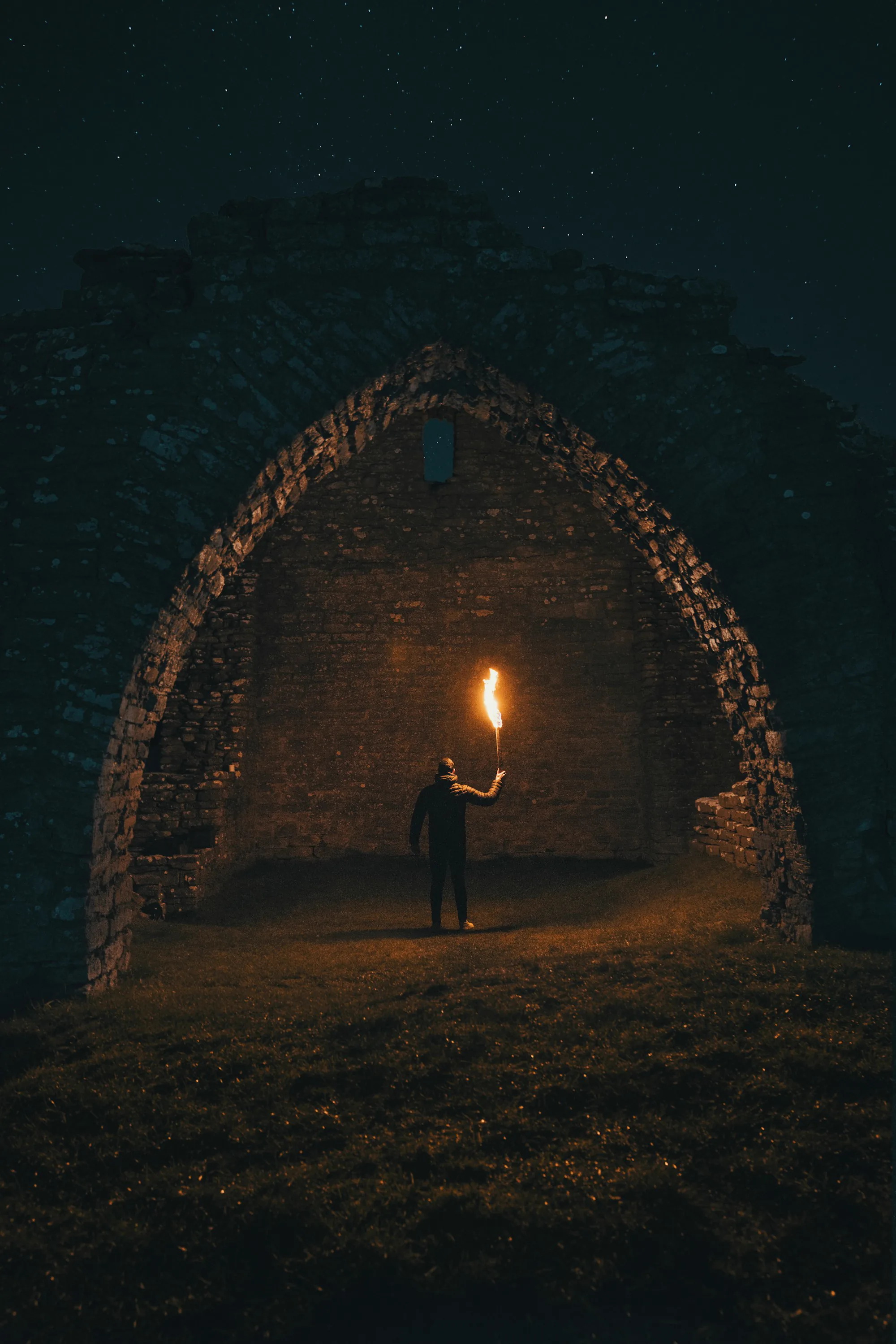 A lone figure holding a flaming torch inside a dark stone archway