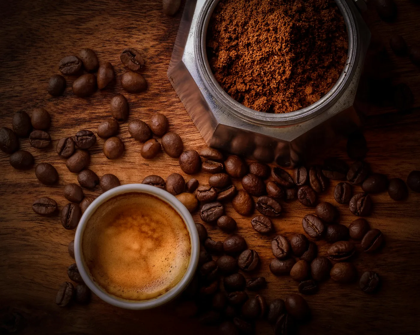 Dark roasted coffee beans and an espresso on a dark wooden surface